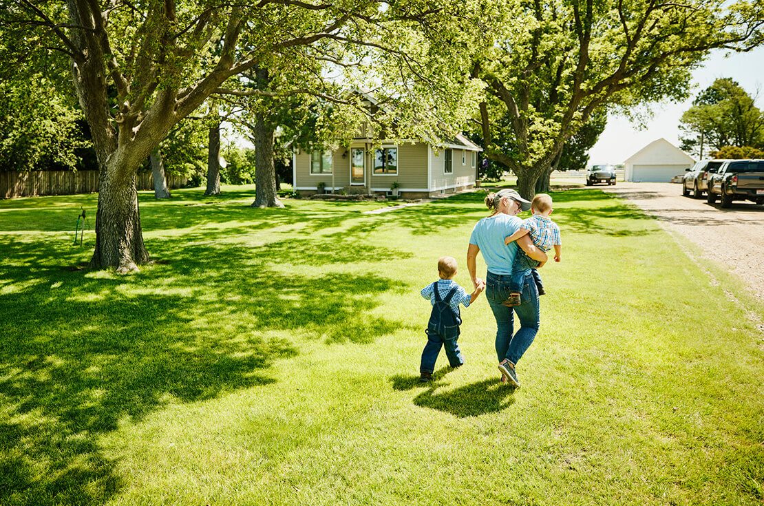 Wide shot rear view of grandmother walking with grandsons through front yard of home